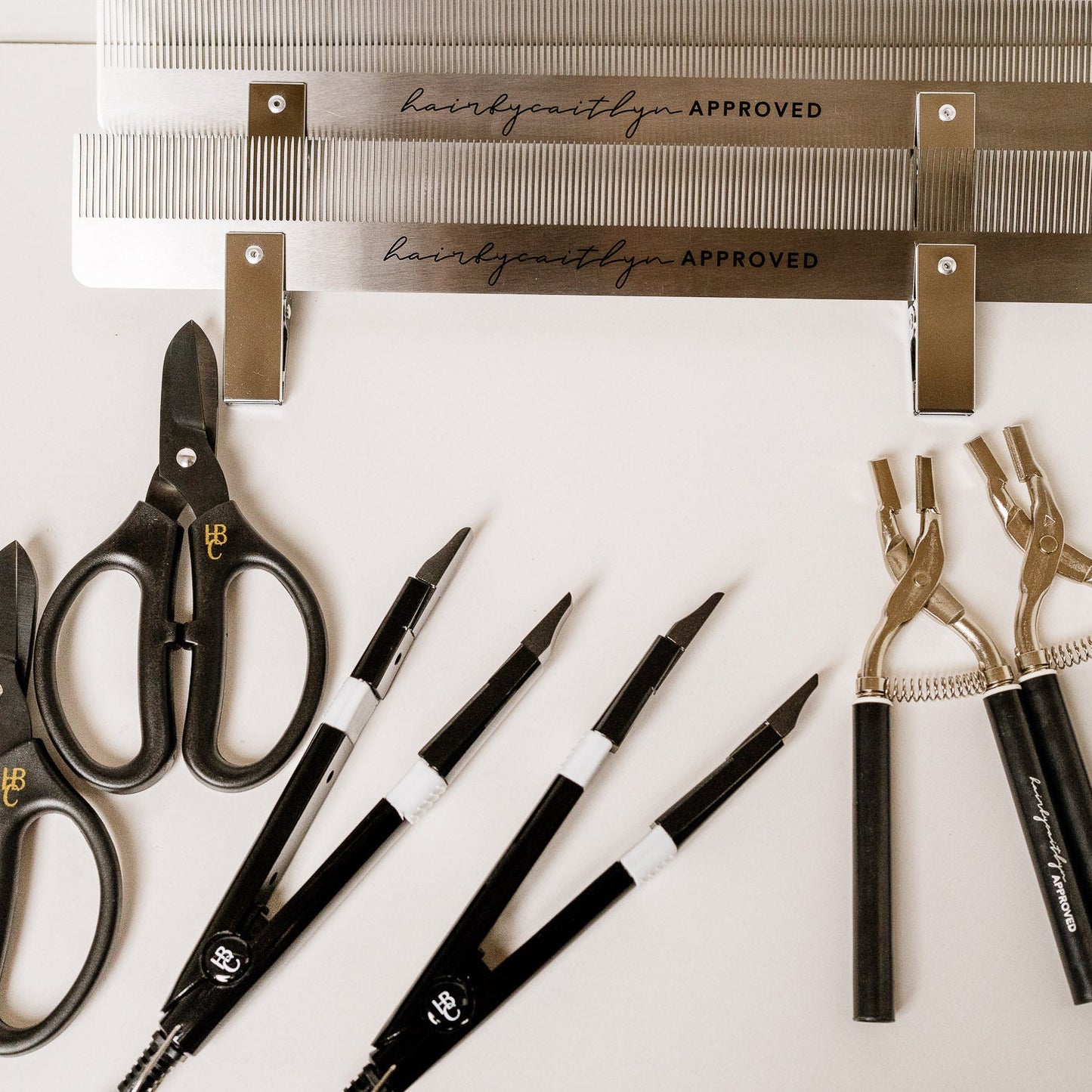 A collection of hair extension tools including combs, scissors, and pliers laid out on a white surface.