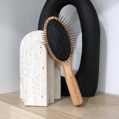 Wooden hairbrush with rounded metal pin bristles on a textured stone stand against a neutral background