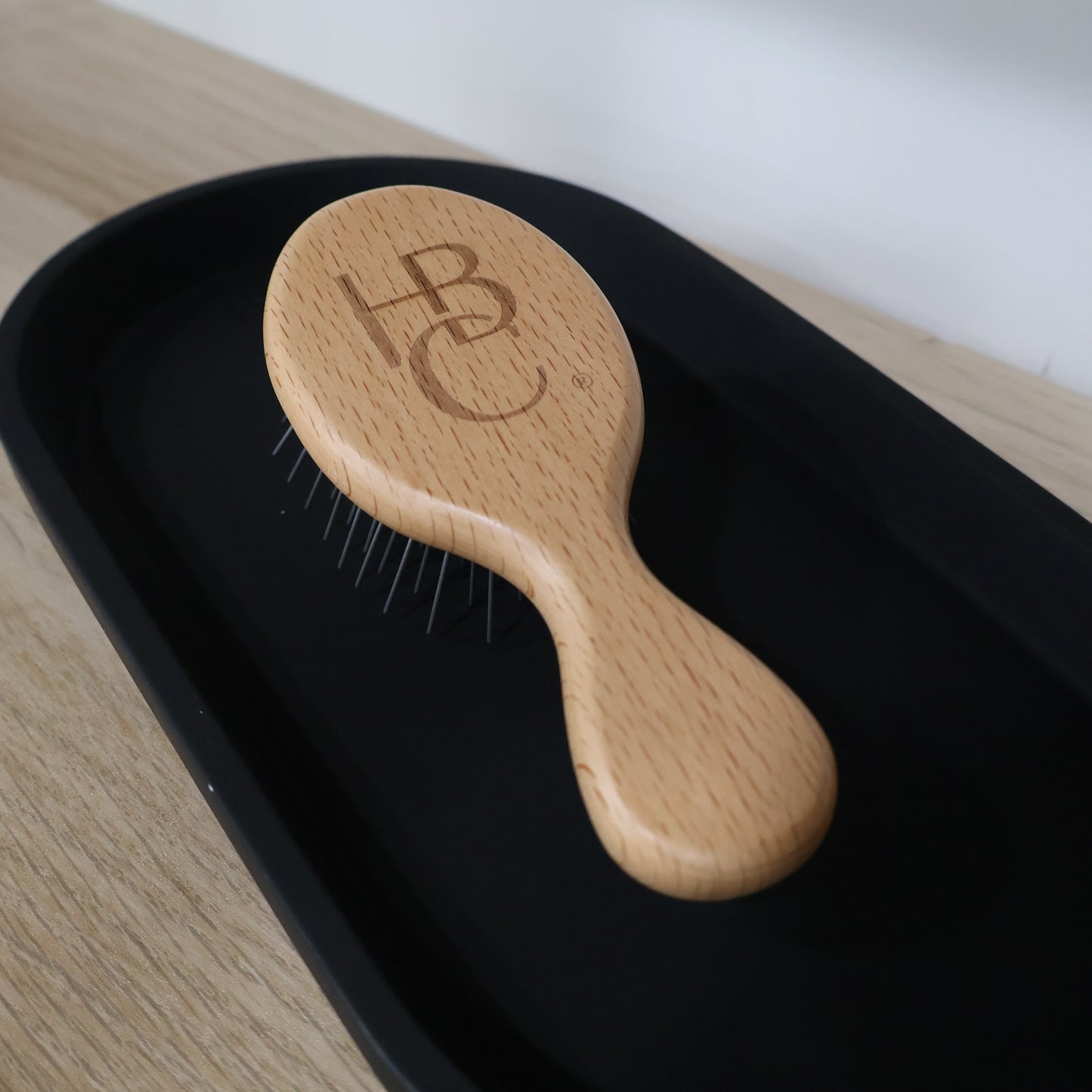 Wooden hairbrush with 'HBC' logo on a black tray