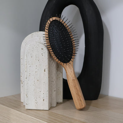 Wooden hairbrush with metal pin bristles on a textured stone stand against a neutral background