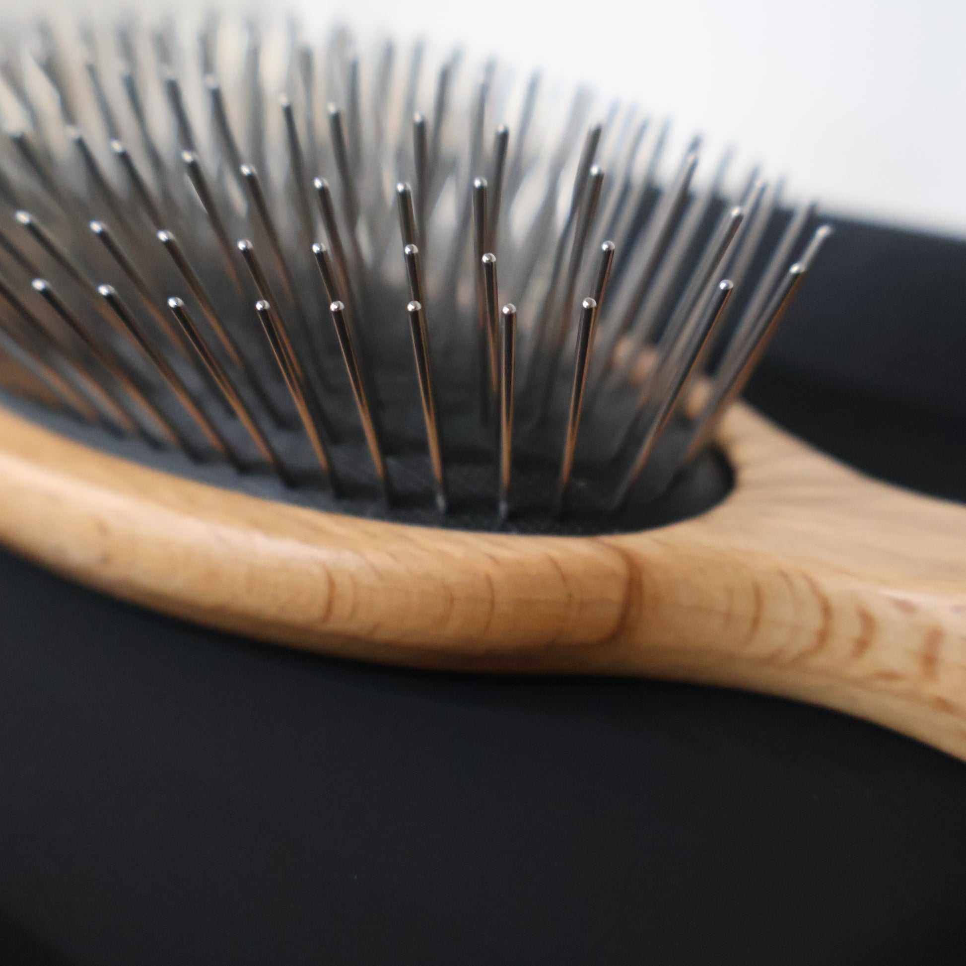 Close-up of a hairbrush with wooden handle and metal bristles on a black background