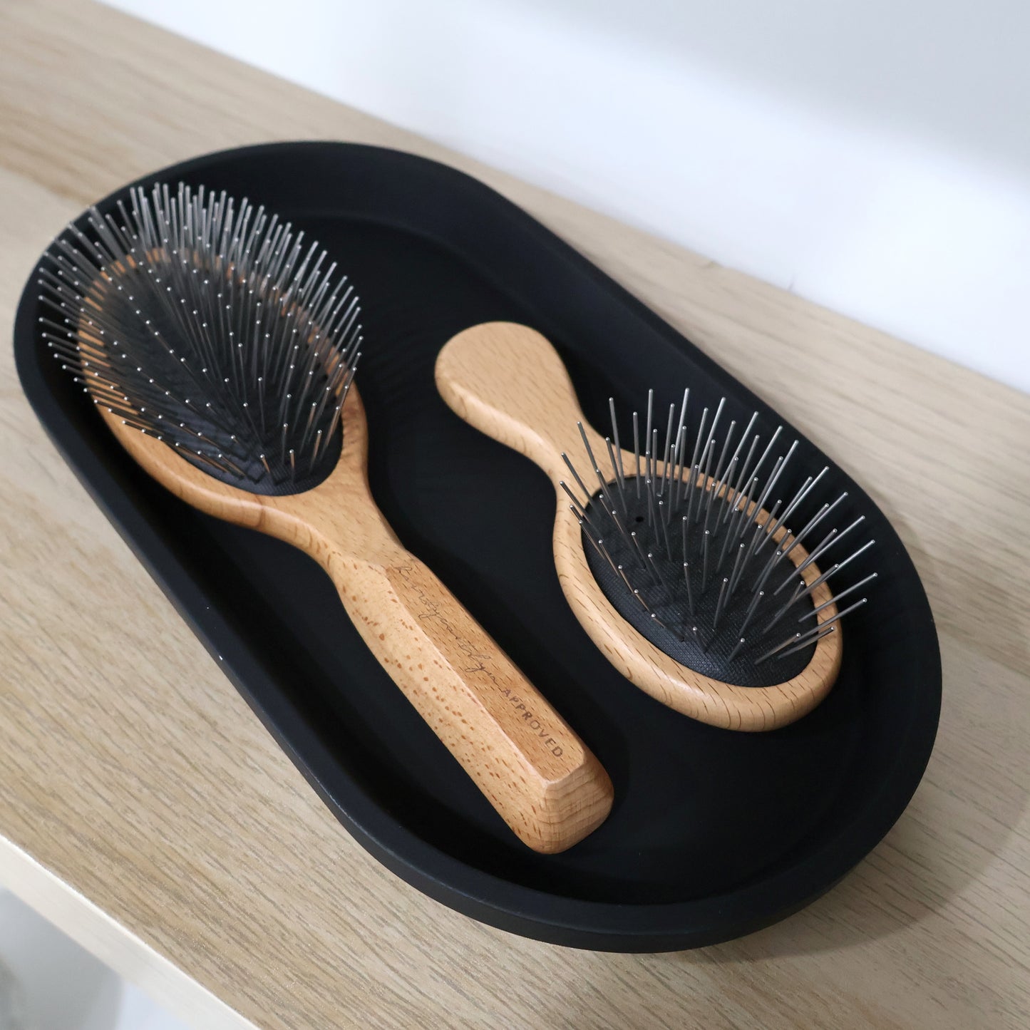 Two wooden hairbrushes on a black tray with a white background