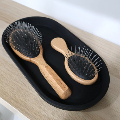 Two wooden hairbrushes on a black tray with a white background