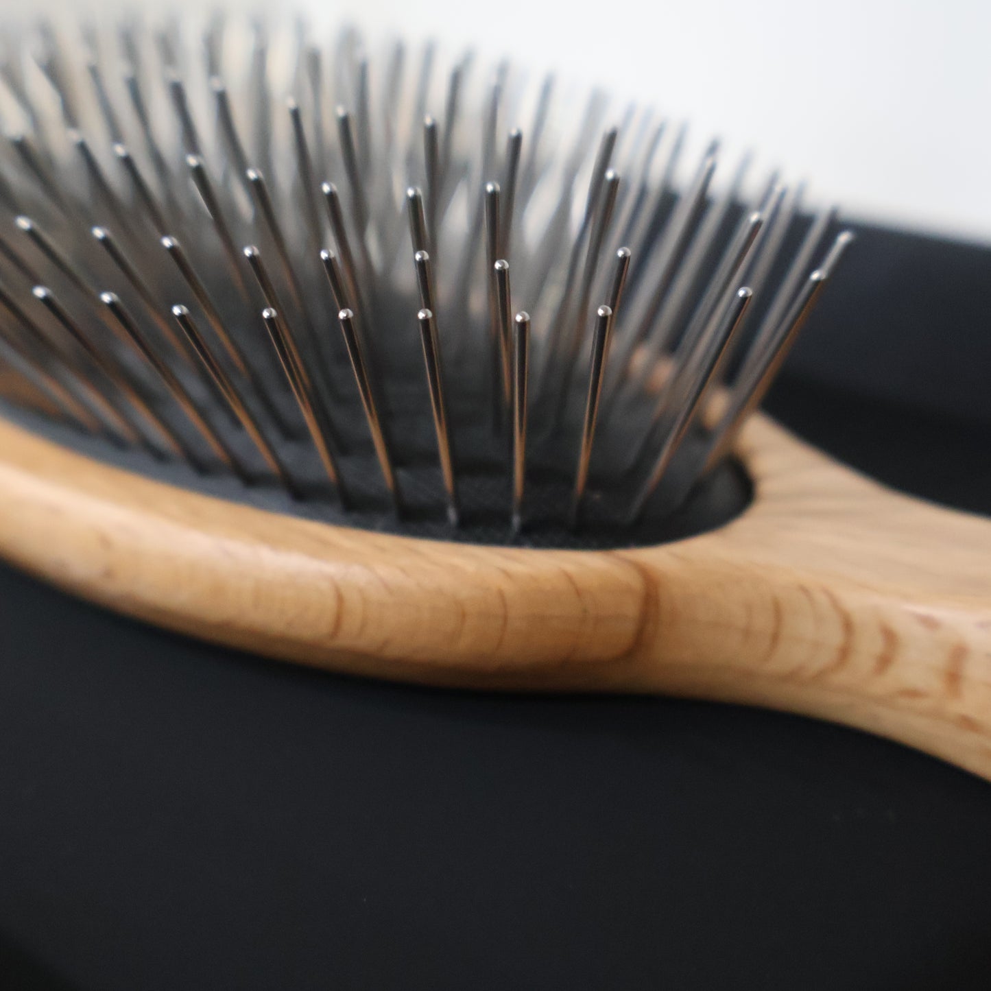 Close-up of a hairbrush with wooden handle and metal bristles on a black background