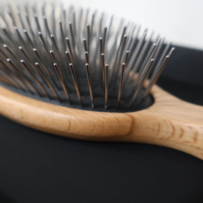 Close-up of a hairbrush with wooden handle and metal bristles on a black background