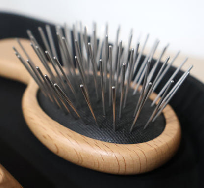 small travel size Wooden hairbrush with metal pin bristles on a black background.