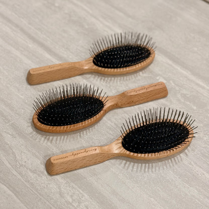 Three wooden hairbrushes with black bristles on a light wooden surface