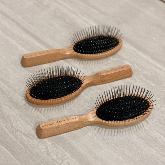 Three wooden hairbrushes with black bristles on a light wooden surface