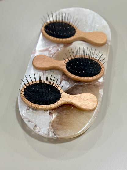 Three wooden hairbrushes with black bristles on a white stone surface